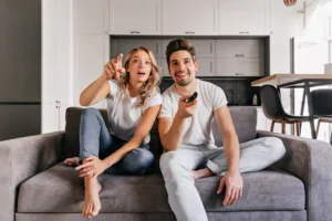 Happy couple on gray sofa with TV remote, enjoying entertainment content through iptv pro service at home