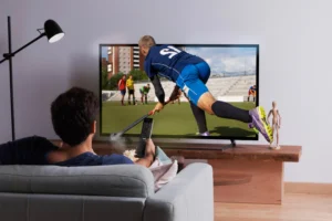 Man watching field hockey match on TV with remote control, streaming sports content from reliable iptv provider